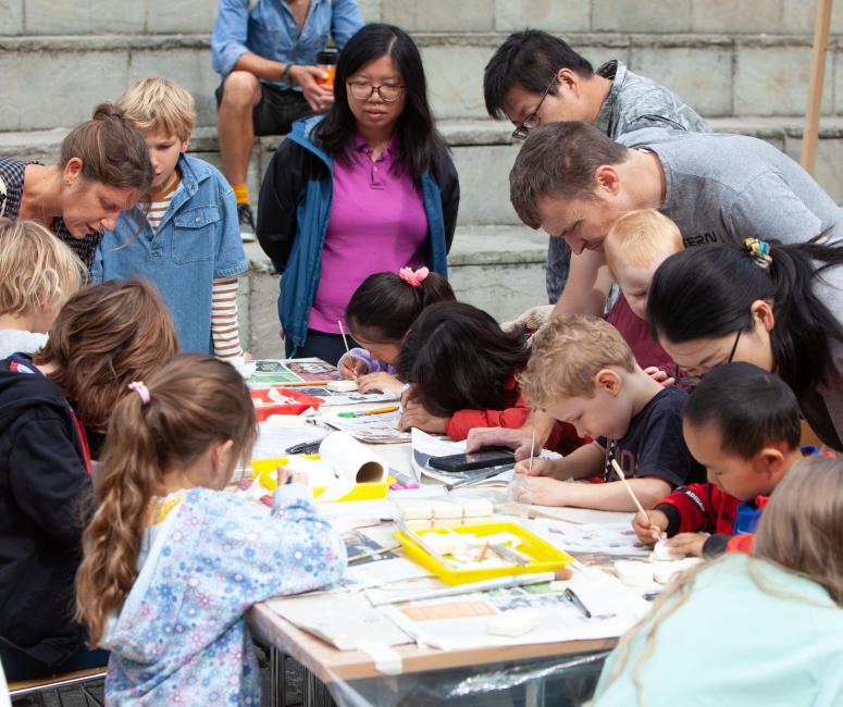 Children sitting round a table carving soap with adults leaning over to help them.