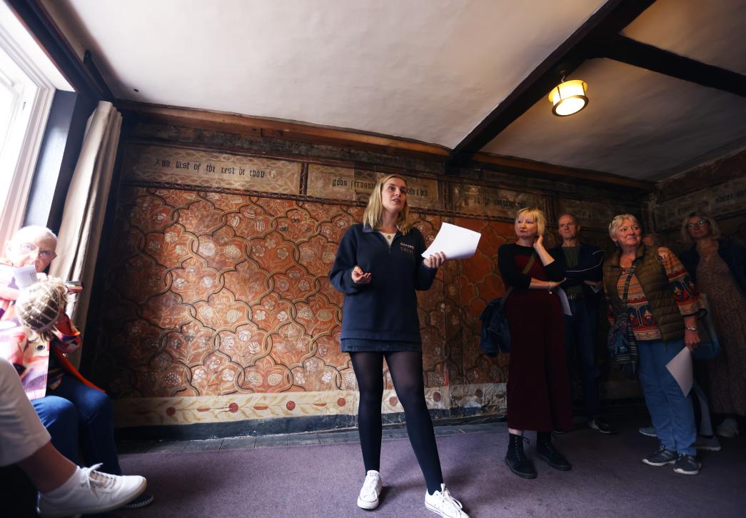 A woman standing in the painted room with a sheet of paper in her hand, talking to visitors.