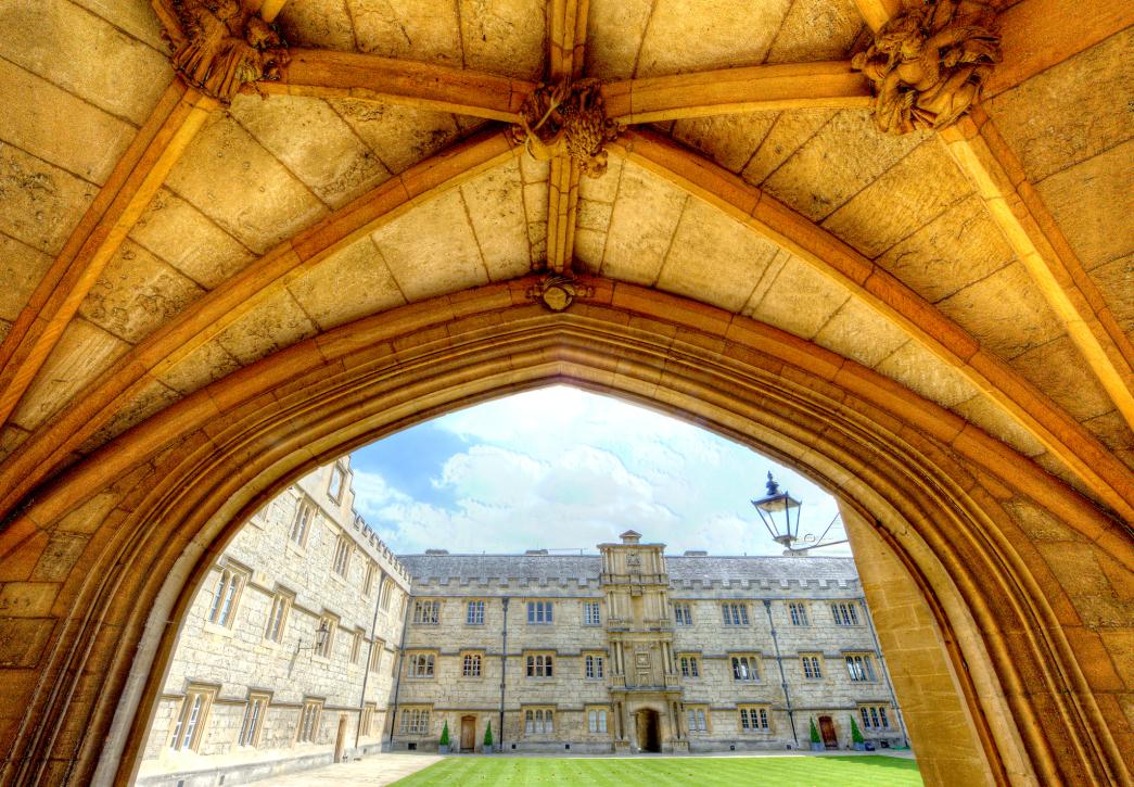 A quadrangle surrounded by a stone building, viewed from beneath a stone archway.